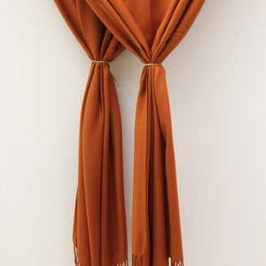 May include: A rust-colored scarf with long fringe on the ends. The scarf is folded in half and tied together with a string.