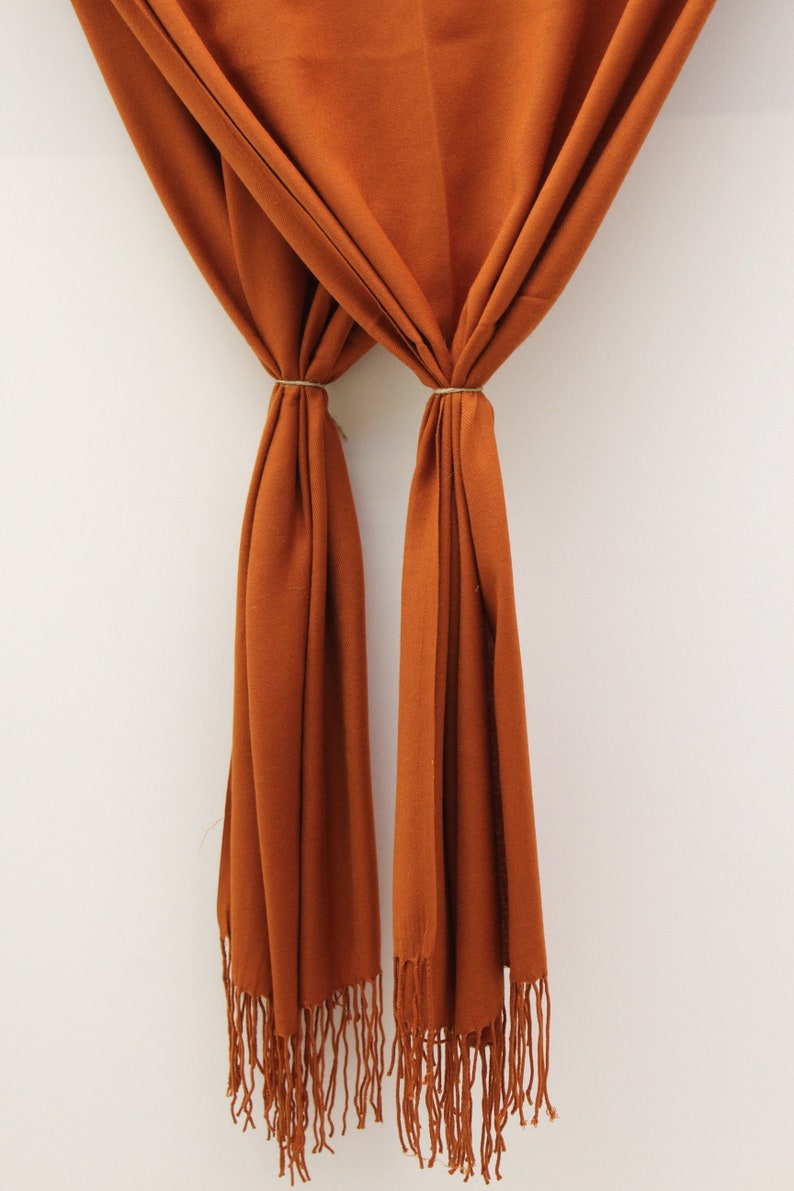 May include: A rust-colored scarf with long fringe on the ends. The scarf is folded in half and tied together with a string.