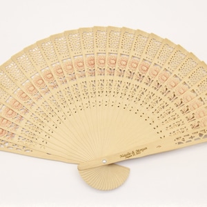 May include: A light brown wooden hand fan with a floral design and the text "Natalie & Morgan June 2021" engraved on the handle.