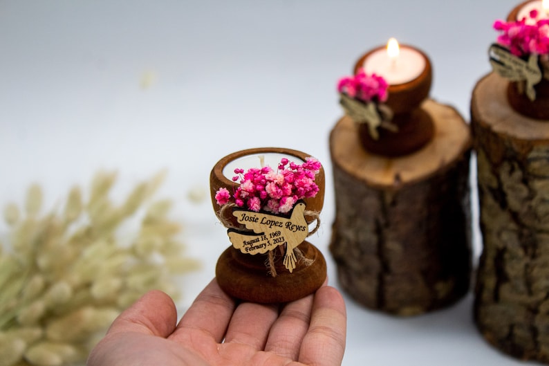 May include: A small wooden candle holder with a white candle and pink flowers. A wooden dove with the text "Josie Lopez Reyes August 1st, 1969 February 3, 2023" is attached to the holder.