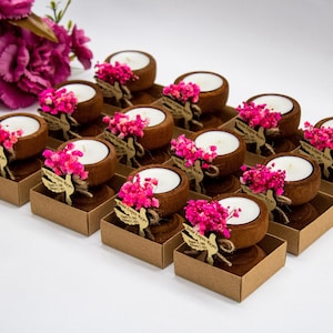May include: A set of 15 small wooden candle holders with pink dried flowers and a white candle in each. The holders are arranged in rows on a white surface.