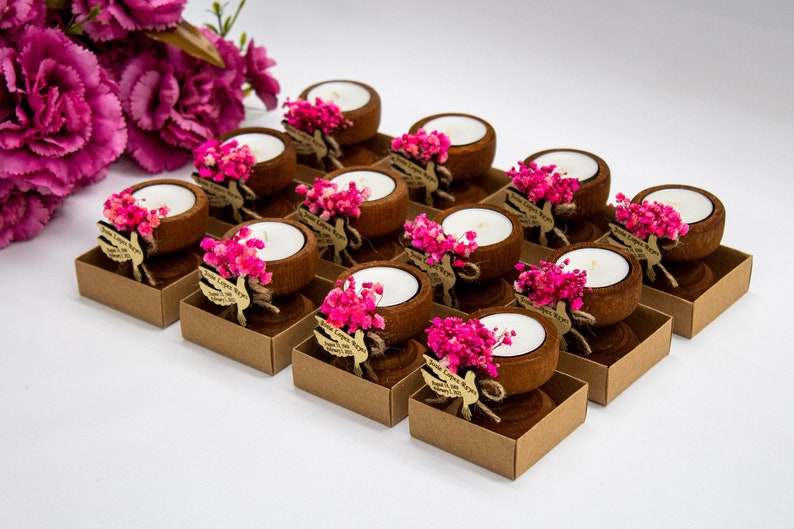 May include: A set of 15 small wooden candle holders with pink dried flowers and a white candle in each. The holders are arranged in rows on a white surface.