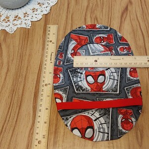 May include: A gray and red fabric circle with a repeating pattern of Spiderman's face in a comic book style. The fabric has a red trim around the edge. The circle is approximately 7 inches in diameter.