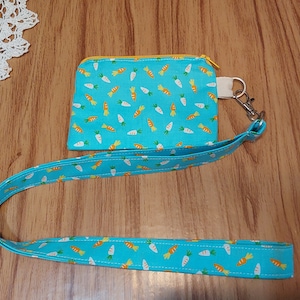 May include: A turquoise blue lanyard with a matching zippered pouch featuring a white and orange carrot pattern. The lanyard has a silver clip and the pouch has a yellow zipper.