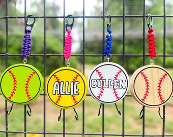 Könnte beinhalten: Vier personalisierte Softball-förmige Haken mit verschiedenen Namen, "Allie", "Cullen" und zwei leere Haken. Jeder Haken ist an einem bunten geflochtenen Seil mit einem Metallclip befestigt.