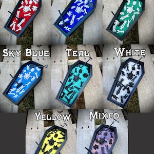 May include: Coffin-shaped trinket dish filled with tiny skeleton figurines. The dishes are available in red, royal blue, sea green, sky blue, teal, white, yellow, and mixed colors.