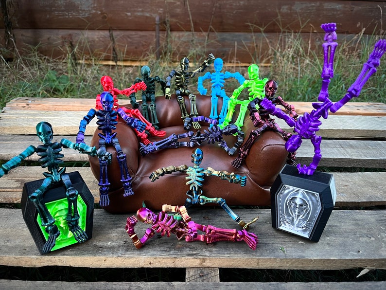 May include: A group of colorful articulated skeleton figures in various poses, some sitting on a brown couch, others standing on a wooden surface. The skeletons are made of plastic and have a variety of colors, including red, blue, green, purple, and yellow.