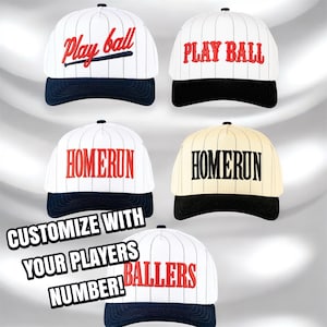 Puede incluir: Gorras de béisbol blancas y azul marino con textos como "Play Ball" y "Homerun". Algunas gorras tienen rayas. También se ve el texto "Customize with your players number!"