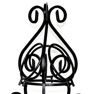 May include: Black metal plant stand with a decorative, ornate design. The stand has a round top and three legs with swirling details.
