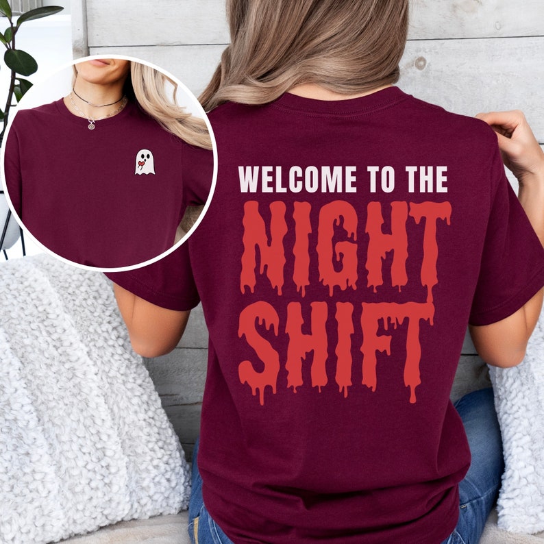 Peut inclure: Un t-shirt bordeaux avec le texte "Welcome to the Night Shift" en lettres rouges qui coulent. Un petit fant&ocirc;me blanc avec un c&oelig;ur rouge est sur le devant du t-shirt.