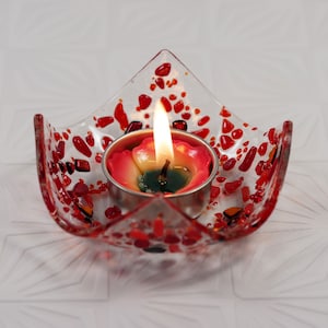 May include: A red glass candle holder with a small, white candle burning inside. The holder has a unique, speckled design.