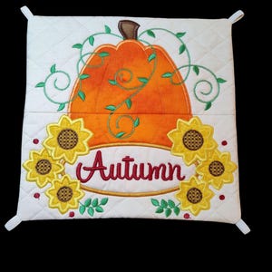 May include: White quilted pot holder with an embroidered orange pumpkin, green vines, yellow sunflowers, and the word "Autumn" in red.