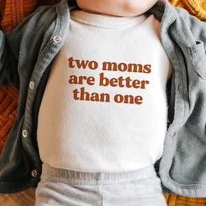 May include: A white baby onesie with the text "two moms are better than one" printed in brown.