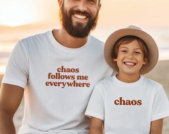 May include: Two people wearing white t-shirts with brown text. The adult's shirt says "chaos follows me everywhere" and the child's shirt says "chaos".