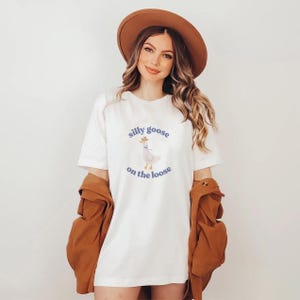 May include: White t-shirt with a cartoon goose wearing a cowboy hat and the text "silly goose on the loose".