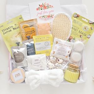 May include: A self-care gift box with skincare products, tea, and a candle. The box includes a Vitamin C serum mask, coconut oil mask, and a card that says "just for you". The box also contains a loofah.