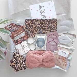 May include: A self-care gift box containing a leopard print cosmetic bag, pink headband, coffee body scrub, bath salts, tea bags, eye and lip masks, and a card with the text "You Got This". A thoughtful present.