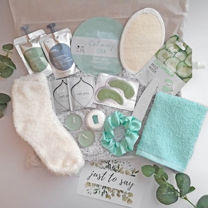 May include: A gift box filled with self-care items, including a white fluffy slipper sock, green eye masks, a green face mask, a green bath towel, a green hair scrunchie, and a card that says "just to say".