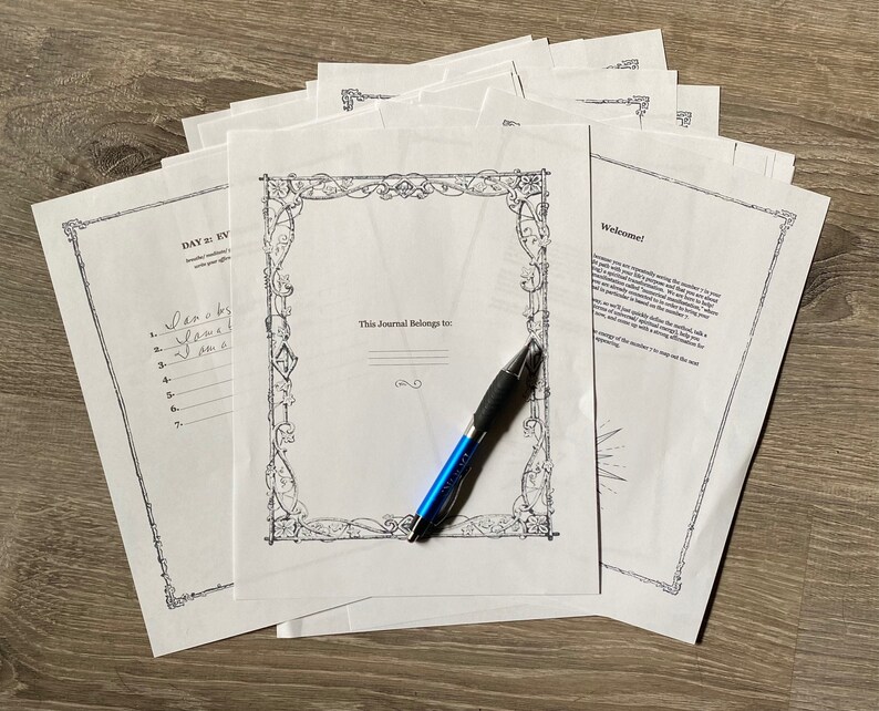 May include: A stack of blank journal pages with a decorative border and the text "This Journal Belongs to:"  A blue pen is lying on top of the pages. The top page has the text "Welcome!" and a welcome message.