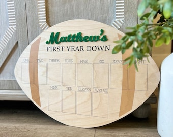 May include: A wooden football-shaped growth chart with the text "Matthew's First Year Down" and numbered spaces for each month of the year.