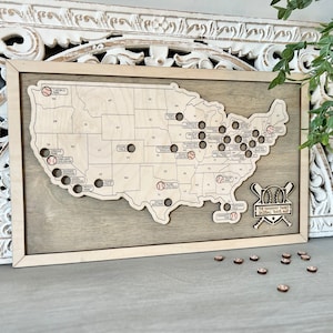 May include: A wooden map of the United States with baseballs marking the location of major league baseball stadiums. The map is framed in wood and has the text "The Baseball Fans Baseball Travel Map" at the bottom.