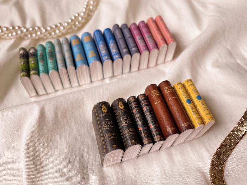 Two rows of books arranged side by side to show the spines. The top row has eight pairs of books arranged in colour order from green to to blue to pink. The bottom row has four pairs arranged from brown to yellow.