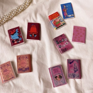 Five pairs of miniature books laid out flat to show the cover. These are all red and pink in colour. Peter pan and wendy. Harry potter and the philosopher's stone. The little princess. Burn book. Beauty and the beast.