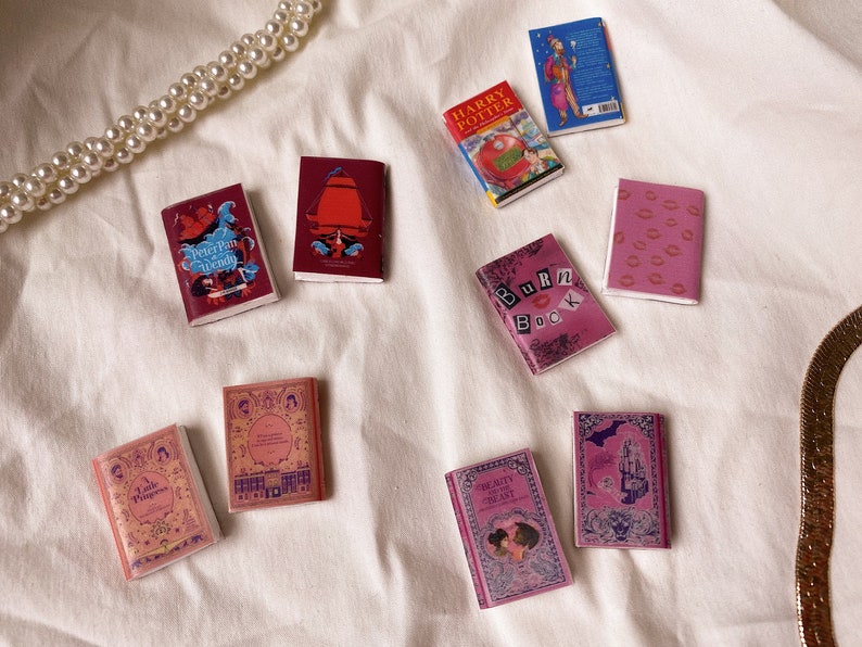 Five pairs of miniature books laid out flat to show the cover. These are all red and pink in colour. Peter pan and wendy. Harry potter and the philosopher's stone. The little princess. Burn book. Beauty and the beast.