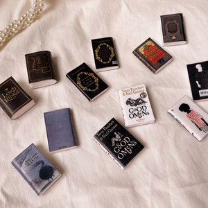 Six pairs of miniature books laid out flat to show the front and back covers. These are all black white or grey in colour. Lord of the rings. The chronicles of narnia. The phantom of the opera. Potion making. Good omens. Noughts and crosses.