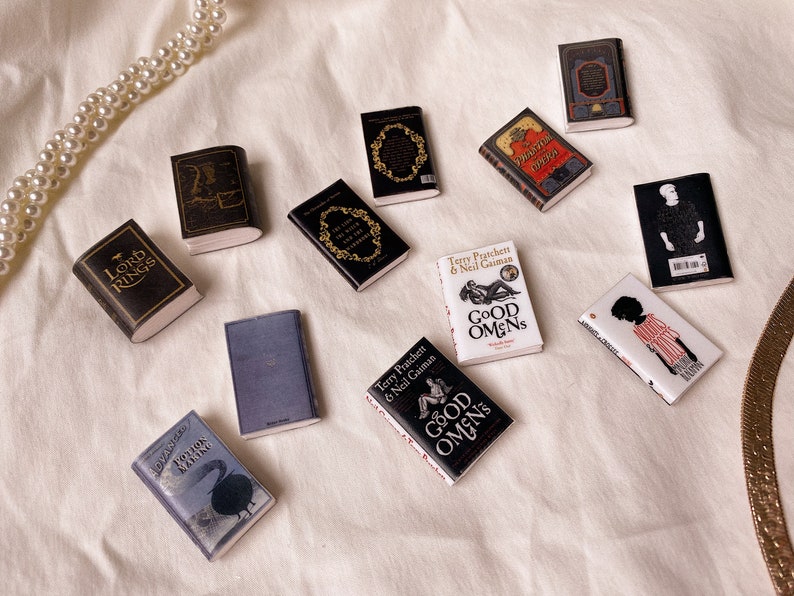 Six pairs of miniature books laid out flat to show the front and back covers. These are all black white or grey in colour. Lord of the rings. The chronicles of narnia. The phantom of the opera. Potion making. Good omens. Noughts and crosses.