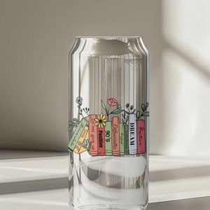 May include: A clear glass can with a stack of colorful books printed on the side. The books have motivational words like "Dream", "Positive", "90's", "Enthusiastic", "Goodness", "Do not give up", and "Smile".