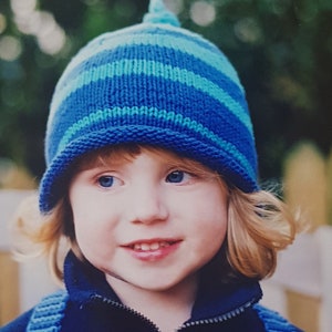 May include: A young child wearing a blue and green striped knitted hat and a blue jacket with blue and green striped straps.