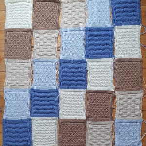 May include: A knitted blanket made of squares in various shades of blue, brown, and white. Each square features a different knit stitch pattern.