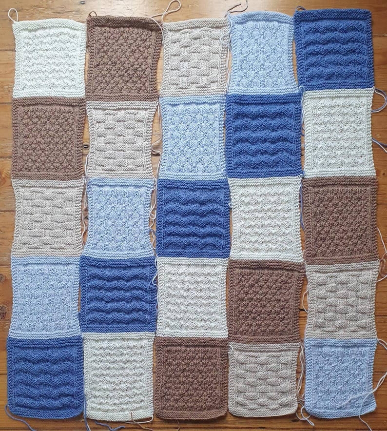 May include: A knitted blanket made of squares in various shades of blue, brown, and white. Each square features a different knit stitch pattern.