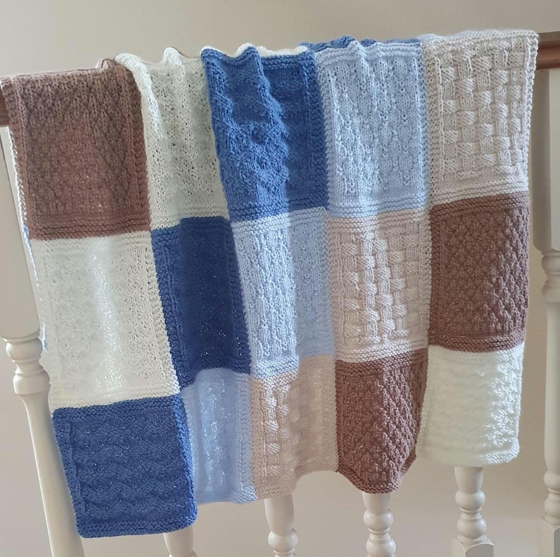 May include: A knitted baby blanket with a patchwork design in shades of blue, brown, and white. The blanket is made of different textures and patterns.