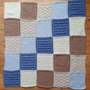 May include: A knitted baby blanket with a patchwork design. The blanket is made up of squares in shades of blue, brown, and white.