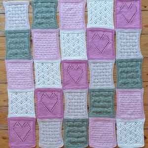 May include: A knitted baby blanket with a patchwork design featuring different textures and colors, including pink, green, and white. The blanket is made up of squares with various patterns, including hearts, diamonds, and dots.
