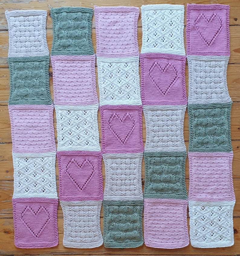 May include: A knitted baby blanket with a patchwork design featuring different textures and colors, including pink, green, and white. The blanket is made up of squares with various patterns, including hearts, diamonds, and dots.