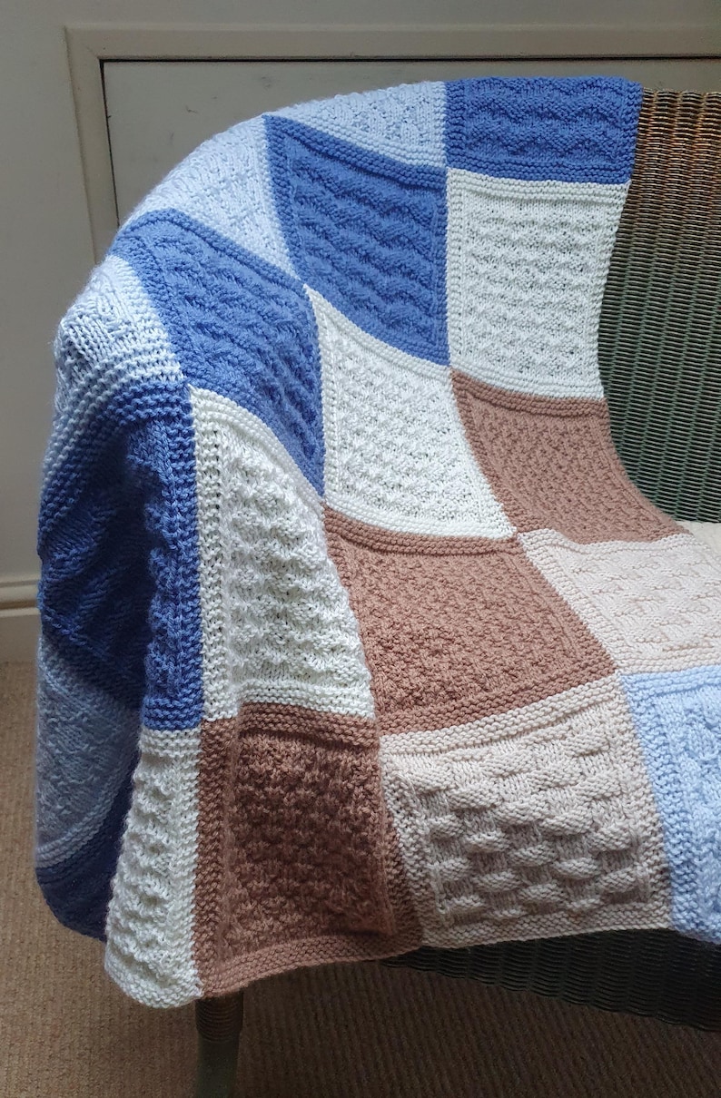 May include: A knitted baby blanket with a patchwork design in shades of blue, white, and brown. The blanket is made of different textures and patterns, creating a unique and cozy look.