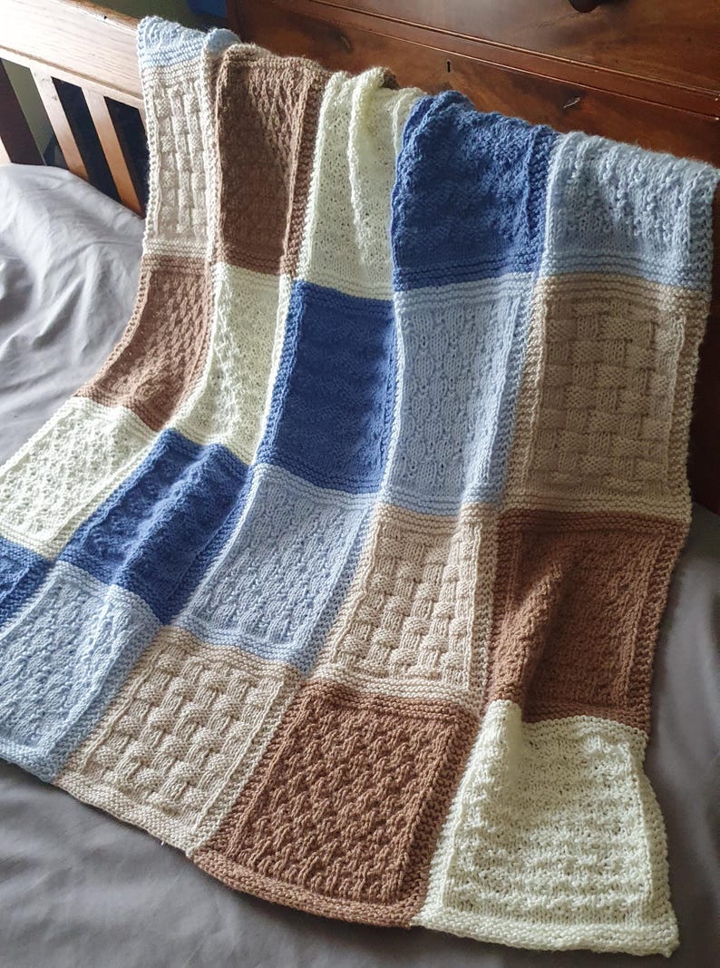 May include: A knitted baby blanket with a patchwork design in shades of blue, brown, and white.