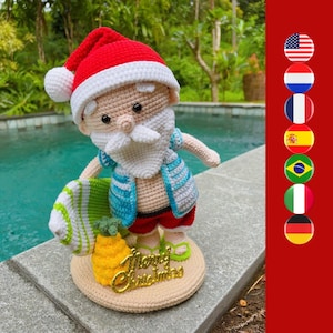May include: A crocheted Santa Claus doll wearing a blue and white striped shirt, red shorts, and a Santa hat. He is holding a green and white surfboard and a yellow pineapple. The doll is standing on a tan crocheted base with the words "Merry Christmas" written in gold.