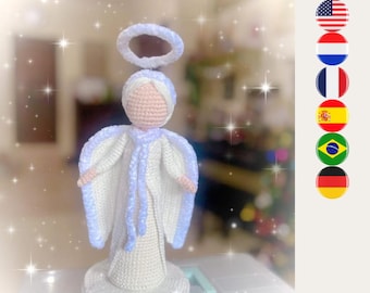 May include: A handcrafted crochet angel figurine featuring a pale pink round head, a white gown with textured light blue trim, and a matching light blue halo positioned above the head. The figure stands on a circular white base with blue accents.