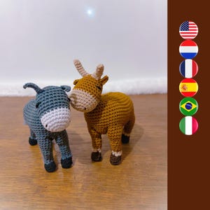 May include: A crocheted brown cow and a crocheted gray donkey. The cow is standing on all four legs and the donkey is standing on its two front legs. The cow and donkey are facing each other.