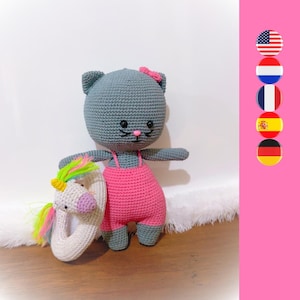 Może przedstawiać: Szara szydełkowa lalka kota w różowym szydełkowym kostiumie kąpielowym trzymająca białą szydełkową dmuchanego jednorożca z tęczowymi akcentami.