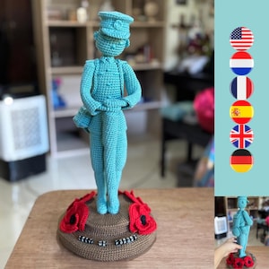 Puede incluir: Una figurita de soldado azul de crochet de pie sobre una base marrón con flores de amapola rojas. La base tiene el texto "Lest We Forget".
