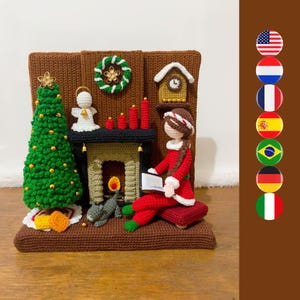 May include: A crocheted holiday scene featuring a brown fireplace, a green Christmas tree with gold beads, a white angel, a grey cat, and a figure in a red outfit reading a book. A clock hangs above the fireplace, which is decorated with red candles.