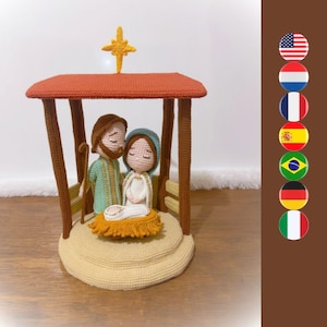 May include: A crochet nativity scene featuring three figures under a brown roof with a yellow star on top. The figures include a bearded person in a green robe, a person in a blue head covering and white robe, and a small figure in a yellow manger.
