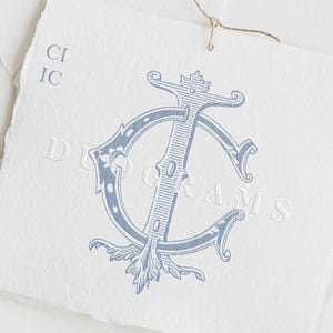 以下が含まれることがあります： 「C」と「I」の文字が絡み合った青と白のモノグラム。モノグラムは装飾的な花のデザインで囲まれています。「DUOGRAMS」というテキストがモノグラムの下に印刷されています。