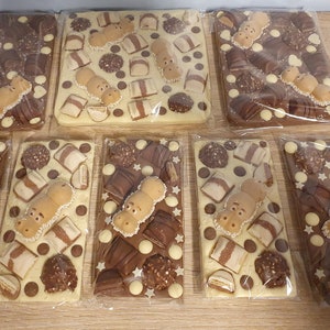May include: Several chocolate bars, each wrapped in clear plastic. The bars are rectangular and topped with various chocolates, including hippo-shaped candies, chocolate pieces, and white chocolate stars. The chocolate bars are on a wooden surface.