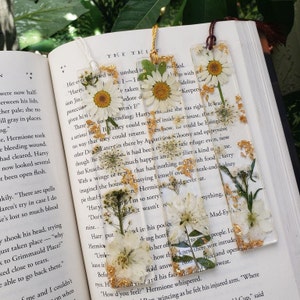 This White Floral bookmark design includes a White Daisy on top, White Queens Lace in the middle, and White Larkspur or another flower at the bottom of the bookmark accompanied by various foliage and gold glitter throughout.
